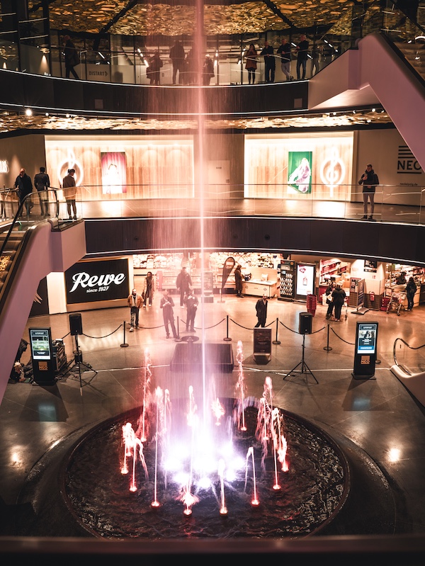 Der Springbrunnen im Lichthof des NEO rot erleuchtet sprudelnd.